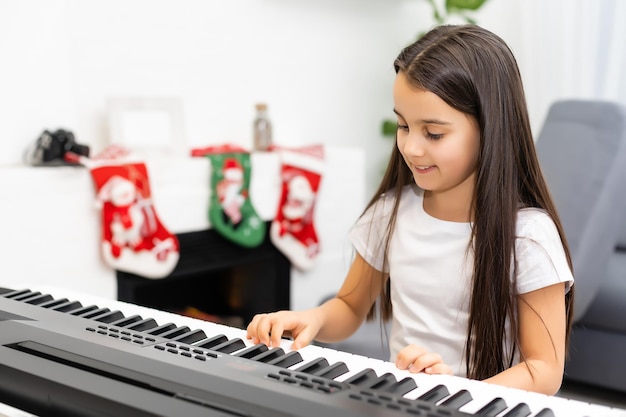 Niña linda tocar melodía navideña en el piano, feliz celebración navideña, felices fiestas de temporada