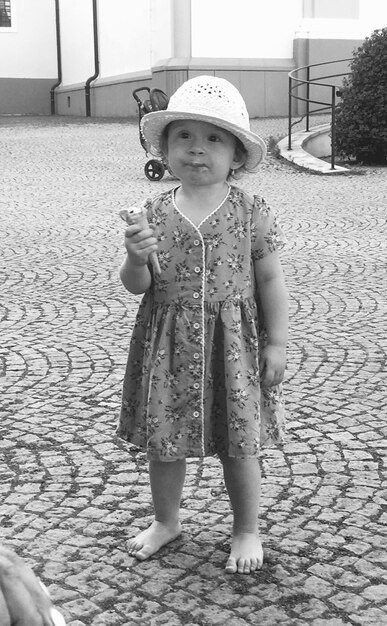 Una niña linda de toda la longitud comiendo un cono de helado mientras está de pie en el sendero