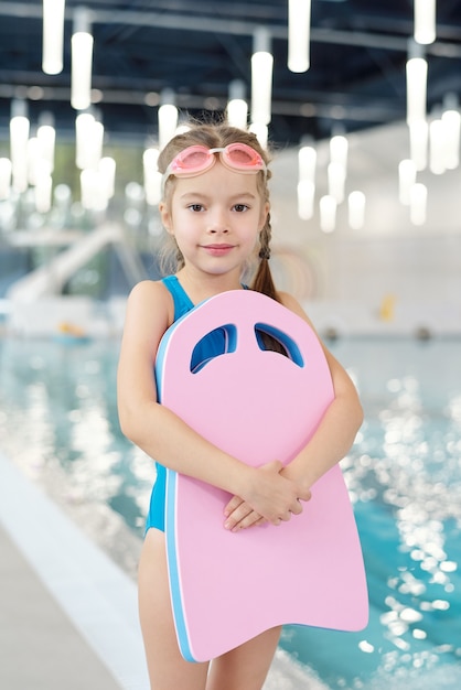 Una niña con gafas de natación de color rosa vestida con un traje de baño  saltando fuera de la piscina