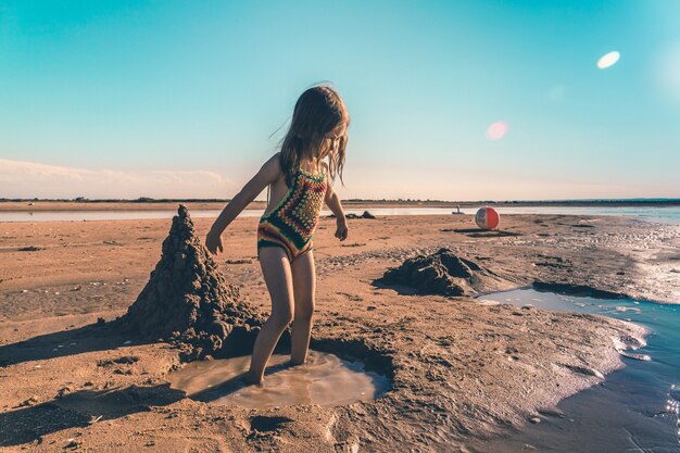 Niña linda en un traje de baño de punto jugando con arena en la orilla del mar.