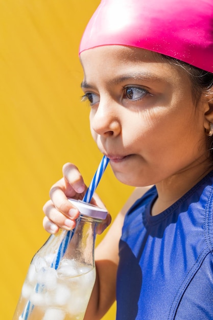 Niña linda en traje de baño tomando el sol mientras toma una limonada