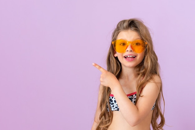 Una niña linda en un traje de baño de verano señala con el dedo hacia un lado