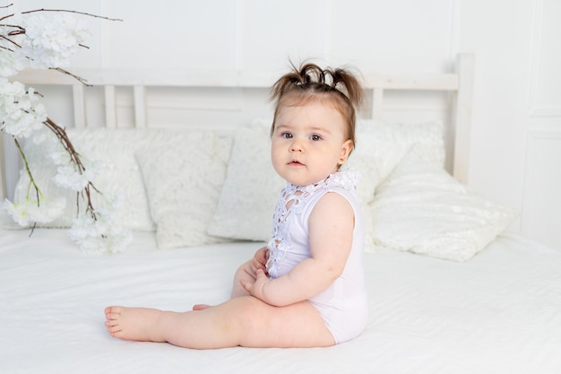 Niña linda en traje blanco en la cama en su casa en una habitación luminosa