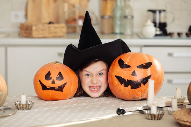 Niña linda en traje de bruja con calabaza tallada