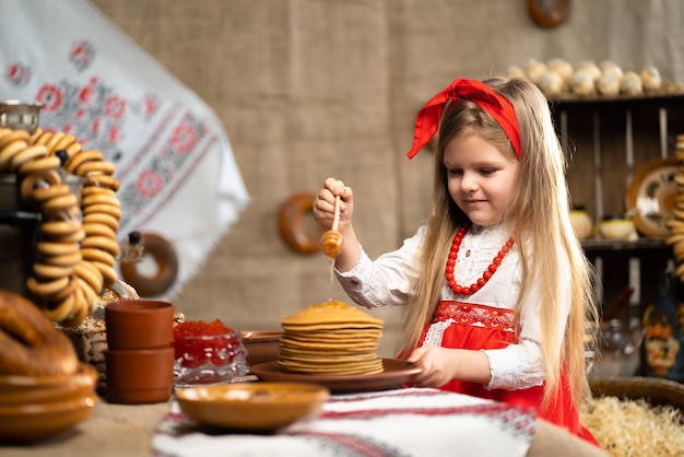 Niña linda en traje folclórico rociadores panqueques con miel mientras celebra Maslenitsa