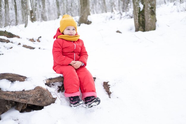 Niña linda en traje de nieve rosa juega con nieve en el bosque de invierno