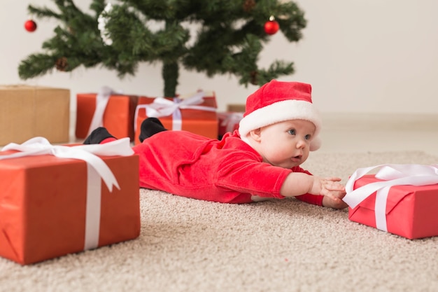 Niña linda con traje de santa claus arrastrándose por el suelo sobre el árbol de Navidad. Temporada de vacaciones.