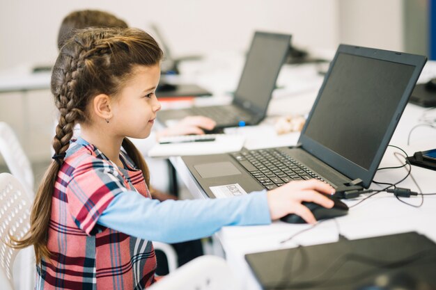 Niña linda usando laptop en el aula