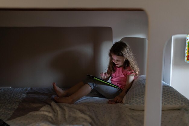 Una niña linda usando una tableta digital en la cama en el dormitorio de su casa