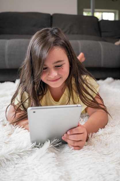 Foto una niña linda ve dibujos animados en una tableta digital el niño yace en el suelo riéndose usando un dispositivo electrónico ocio interior para niños