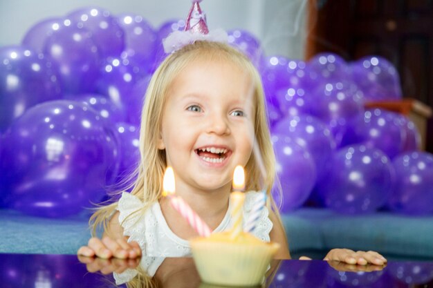 Niña linda en vestido elegante que celebra el día de cumpleaños con globos púrpuras