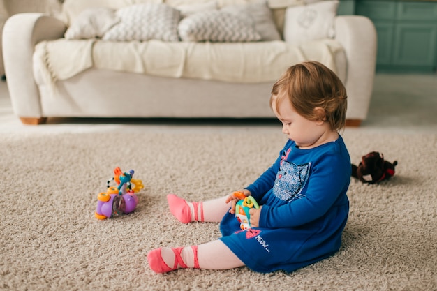 Niña linda en vestido hermoso se sienta en tcarpet y juega con sus diversos juguetes