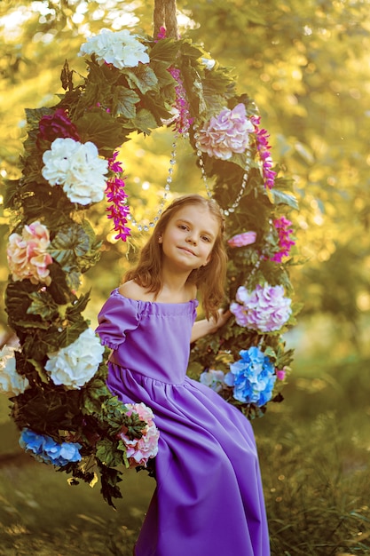 Foto niña linda con vestido lila posando mientras está sentado en el anillo decorado con flores en el parque