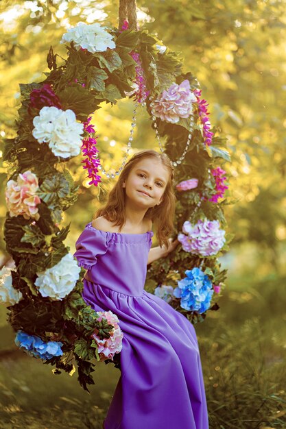 Foto niña linda con vestido lila posando mientras está sentado en el anillo decorado con flores en el verano del parque