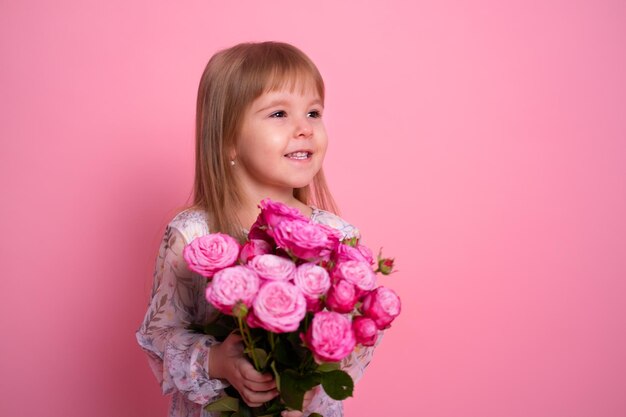 Niña linda en vestido con ramo de rosas rosadas sobre fondo rosa