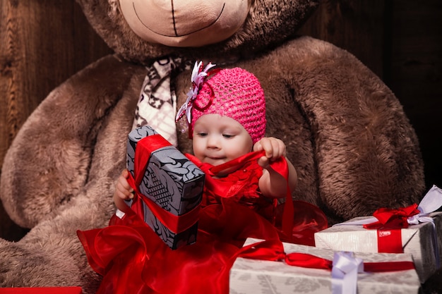 Niña linda en vestido rojo con gran oso de peluche y regalos