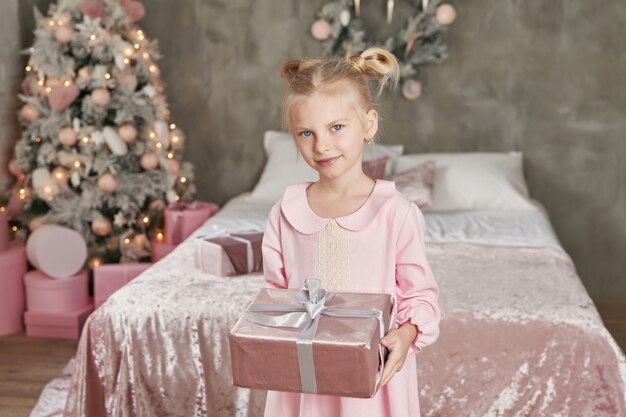 Niña linda en vestido rosa con presente en el fondo Árbol de Navidad. Feliz Navidad y felices fiestas! Bebé sano y concepto de invierno. Familia navidad.