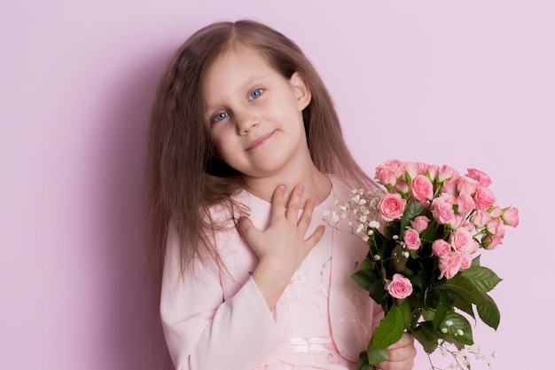 Una niña linda en un vestido rosa sostiene un ramo de rosas rosas