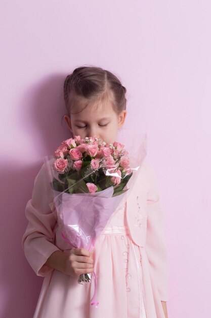 Una niña linda en un vestido rosa sostiene un ramo de rosas rosas