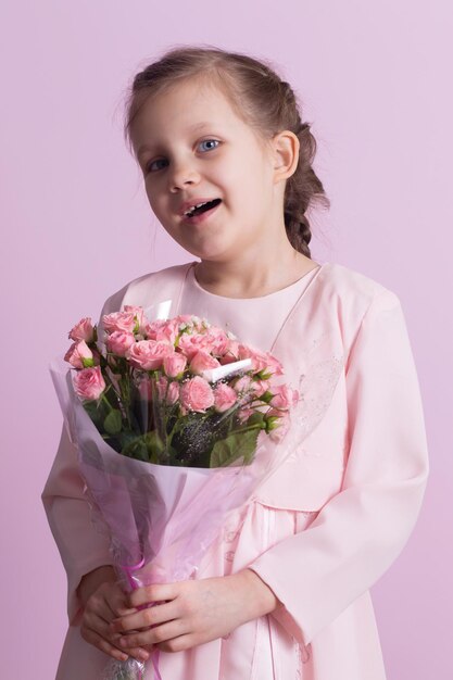 Una niña linda en un vestido rosa sostiene un ramo de rosas rosas