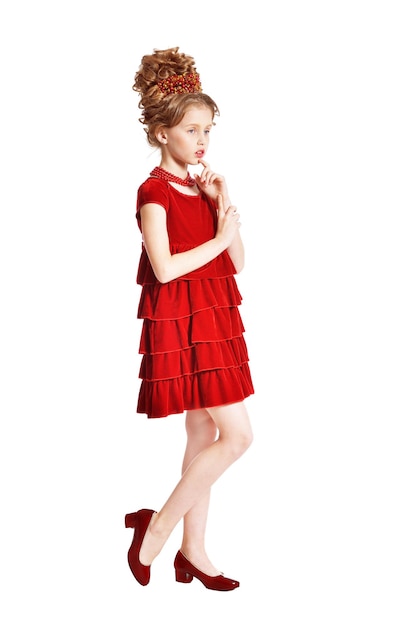 Niña linda en vestido de terciopelo rojo con peinado retro aislado sobre fondo blanco.