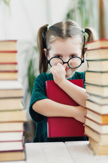 Niña linda con vestido verde con un libro rojo en las manos arreglándose unas gafas en la nariz Concepto de lectura y educación