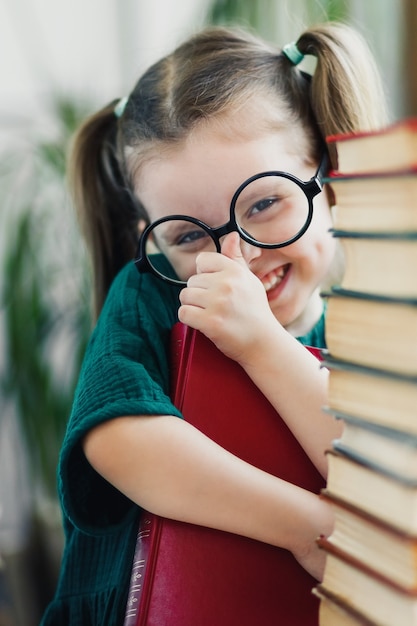 Niña linda en vestido verde con libro rojo en sus manos arreglando unas gafas en su nariz