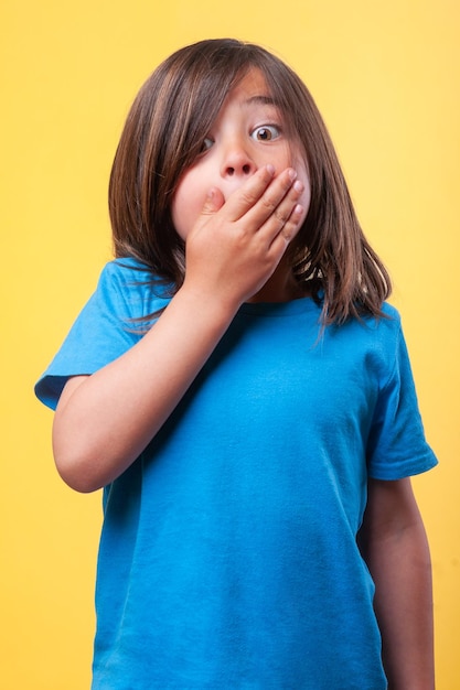 Una niña lleva una camisa azul y se cubre la boca con la mano.