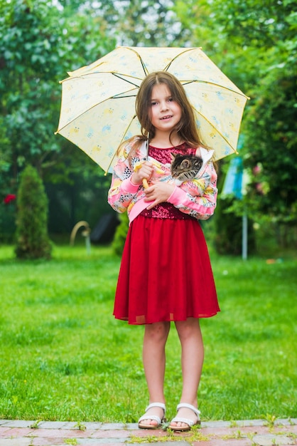 La niña lleva un lindo gatito bajo el concepto de amor y cuidado del paraguas