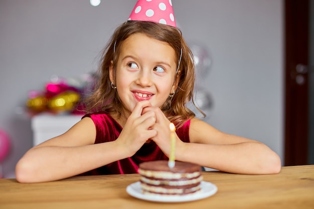 Una niña lleva un sombrero de cumpleaños pide un deseo