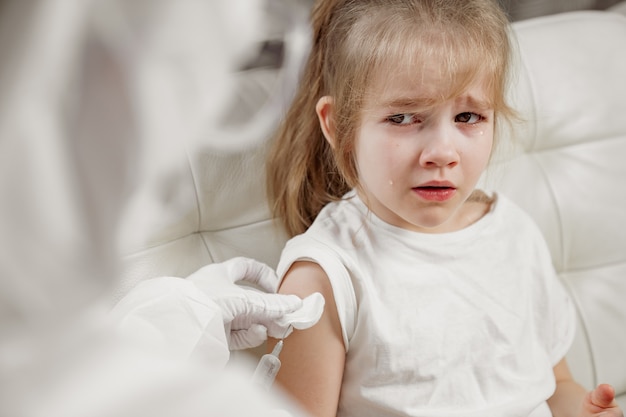 Niña llora herido y asustado. inyección durante la enfermedad. Vacunación. llame al doctor en casa. Pandemia.