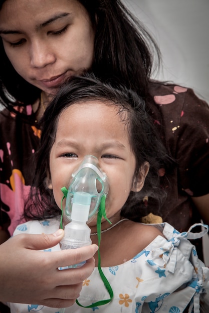 niña llorando al entrar en la máscara de inhalador en el hospital, tono oscuro