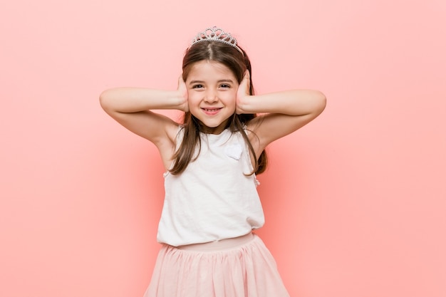 Niña con un look de princesa cubriendo las orejas con las manos tratando de no escuchar un sonido demasiado fuerte.