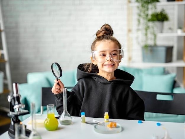 Una niña con una lupa y gafas en la clase de química.