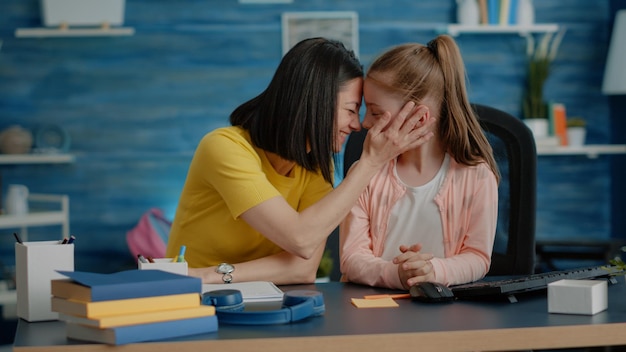 Niña y madre preparándose para cursos escolares en línea, sentados en el escritorio. Padre cariñoso que brinda asistencia y apoyo a un niño pequeño con lecciones y tareas educativas a distancia.