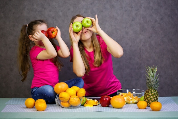Niña con mamá juega con frutas y sonriendo. Vitaminas y nutrición saludable para niños.