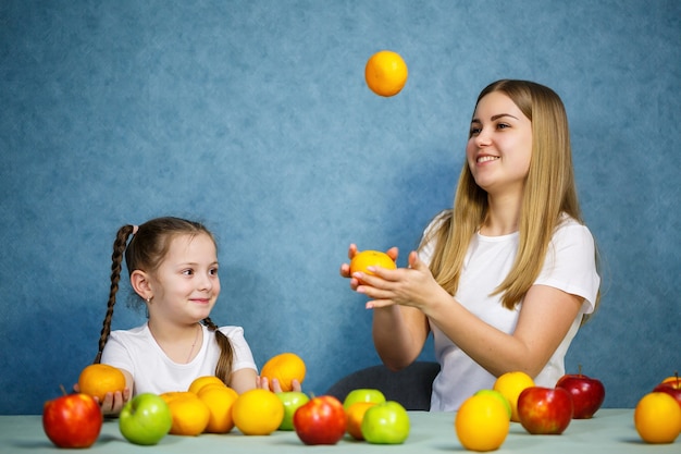 La niña y la mamá juegan con frutas y bromean. Llevan camisetas