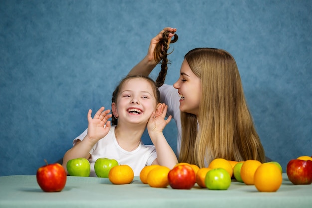 La niña y la mamá juegan con frutas y bromean. Llevan camisetas