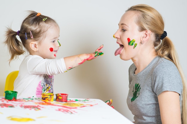 Niña con mamá jugando y jugando con pinturas de colores