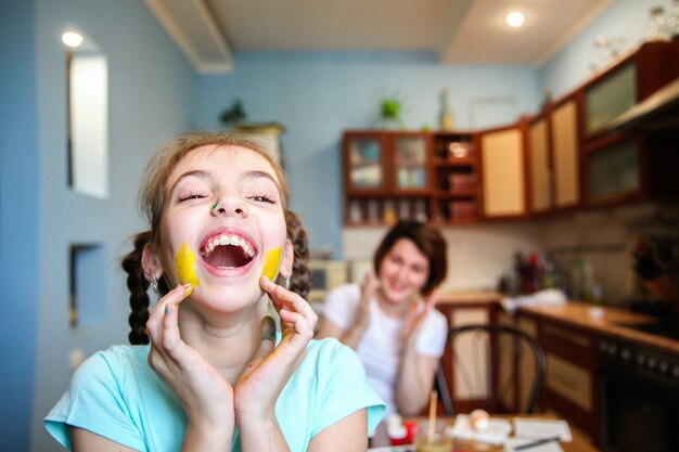 Una niña manchada de pintura con coletas se ríe en la cocina de casa