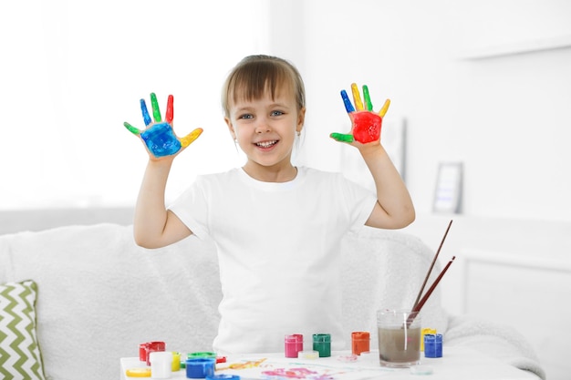 Niña con las manos en pintura sobre fondo interior de casa