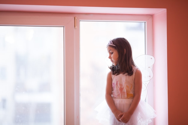 Niña-mariposa en un tutú blanco bailando jugando en el alféizar de la ventana