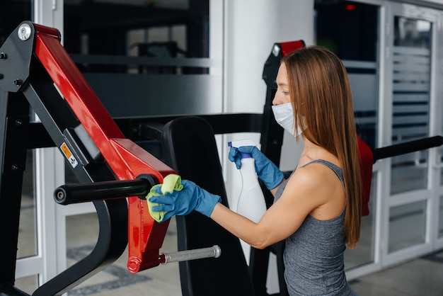 La niña de la máscara desinfectando el equipo del gimnasio durante una pandemia.