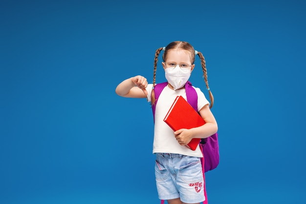 Niña con máscara y gafas con mochila escolar