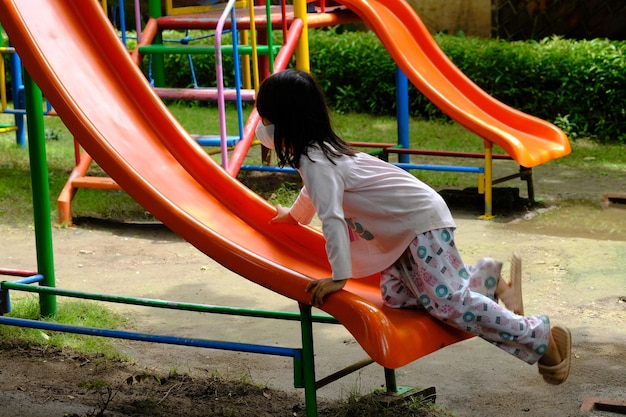 niña con una máscara jugando en el tobogán. la pandemia de covid hizo que todos usaran máscaras. tropical