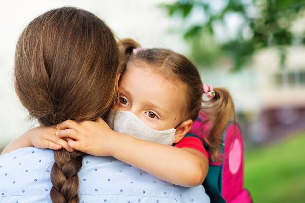 Una niña con máscara médica abraza a su madre antes de la escuela Concepto de cuidado, educación y salud