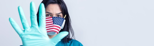 Una niña con una máscara médica y guantes sostiene una bandera estadounidense en sus manos Concepto de coronavirus