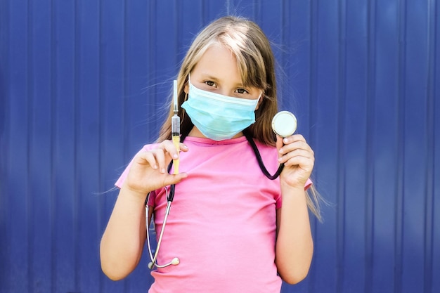 Una niña con una máscara médica juega al doctor sosteniendo una jeringa