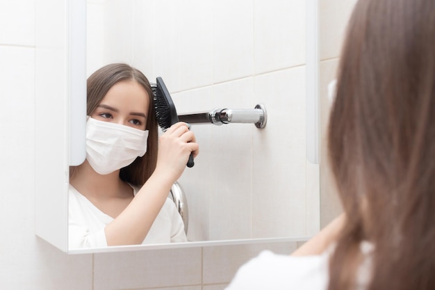 Una niña con una máscara médica se mira en el espejo peinándose Prevención y protección contra enfermedades