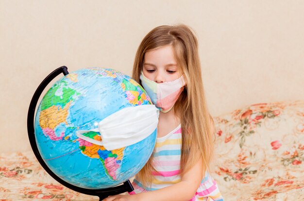 Niña con una máscara médica sostiene un globo en sus manos, envuelto en una máscara médica.